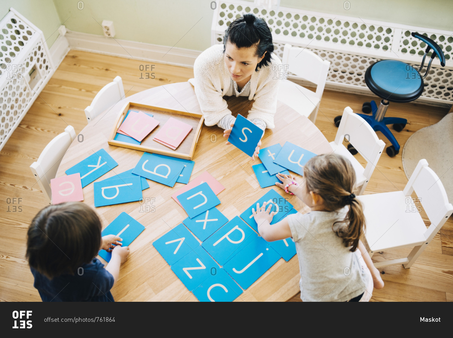 High angle view of confident female teacher showing letter S to students at table in classroom
