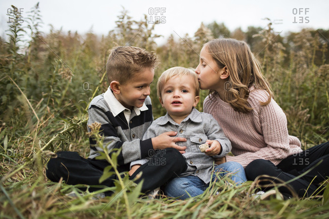 Portrait of cute baby boy with siblings sitting on grassy field in forest