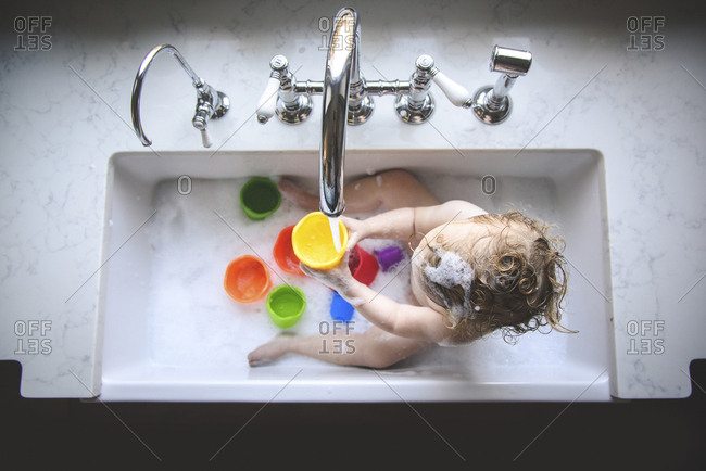 High angle view of naked girl playing with colorful toys while bathing in sink at home