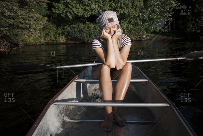 Smiling woman with oar sitting in boat on river against trees at Algonquin Provincial Park