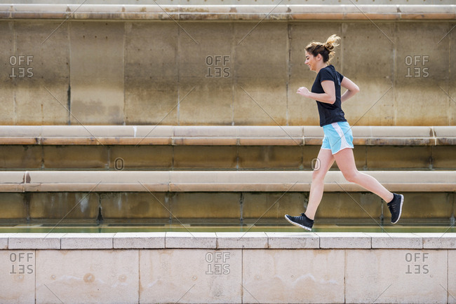 Side view of woman running on retaining wall against wall at park