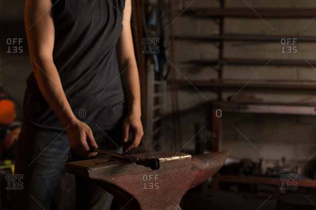 Mid section of female metalsmith holding tool in factory