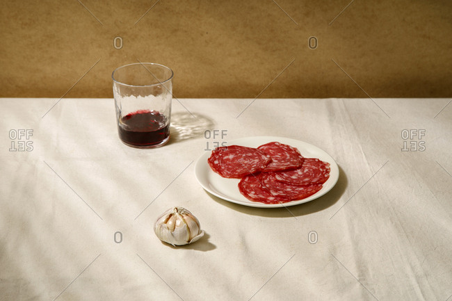 Minimalistic composition with salami slices on a white plate, garlic and a glass of wine