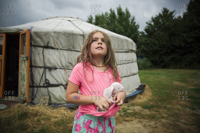 Girl holding a stuffed rabbit looking up toward sky at campground with yurt