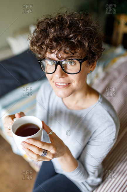 Close up of a woman wearing retro glasses drinking coffee on bed