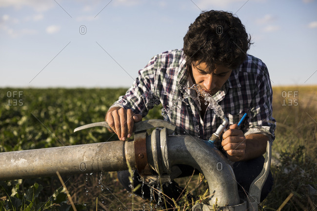 Man in casual outfit drinking from a watering pipe in a farm in Salamanca, Spain