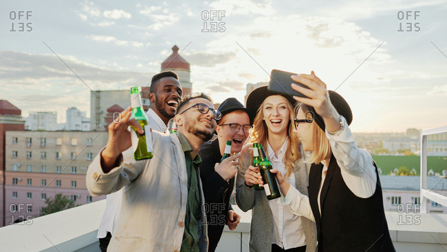 Multiethnic group of young male and female students taking selfie on smartphone and smiling happily while hanging out on rooftop