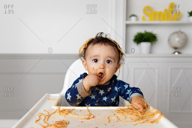 Toddler in high chair making a mess while eating spaghetti