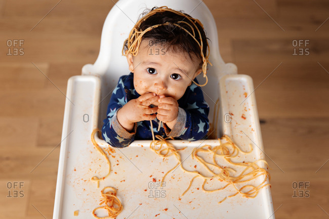 Toddler in high chair looking up while making a mess and eating spaghetti