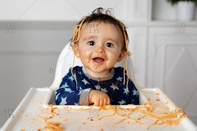 Toddler in high chair making a mess while eating spaghetti