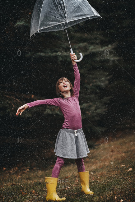 Young girl with an umbrella playing in the falling rain or snow