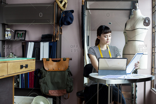 Japanese female fashion designer working in her studio, sitting at table, looking at fabric samples.