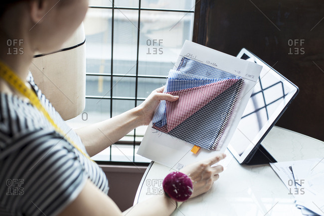 Japanese female fashion designer working in her studio, sitting at table, looking at fabric samples.