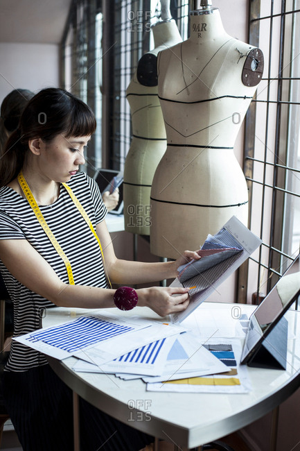 Japanese female fashion designer working in her studio, sitting at table, looking at fabric samples.