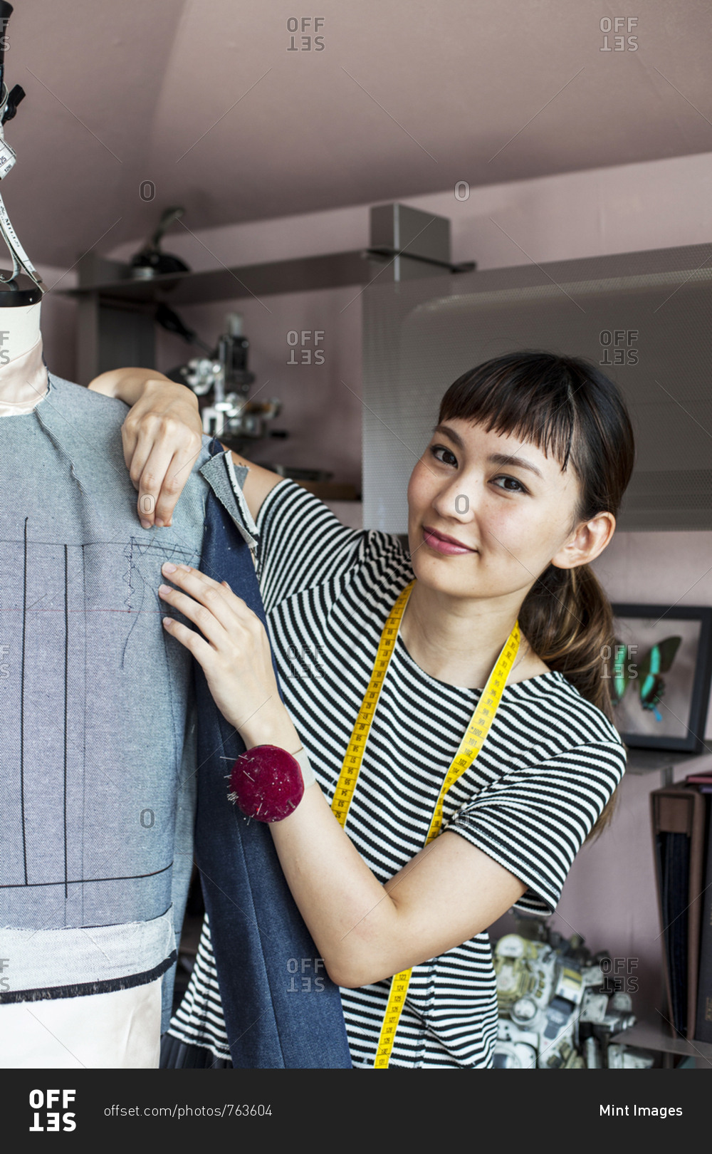 Japanese female fashion designer working on a garment on a dressmaker\'s model in a studio.