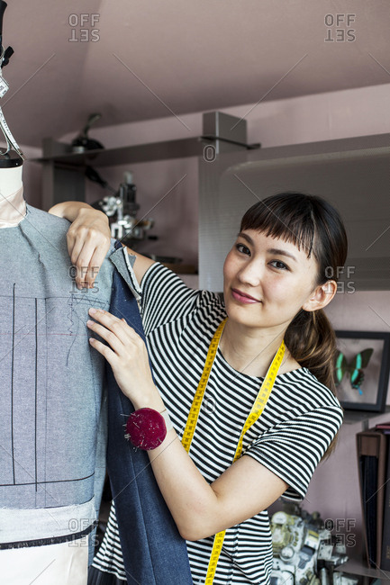 Japanese female fashion designer working on a garment on a dressmaker's model in a studio.