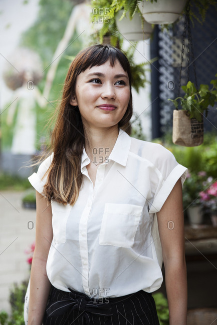 Smiling Japanese woman with long brown hair wearing white short-sleeved blouse standing in a street.