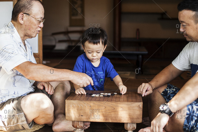 Two Japanese men and little boy sitting on floor on porch of traditional Japanese house, playing Go.