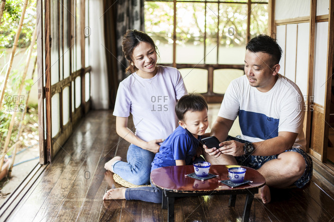 Japanese woman, man and little boy sitting on floor on porch of traditional Japanese house, drinking tea.