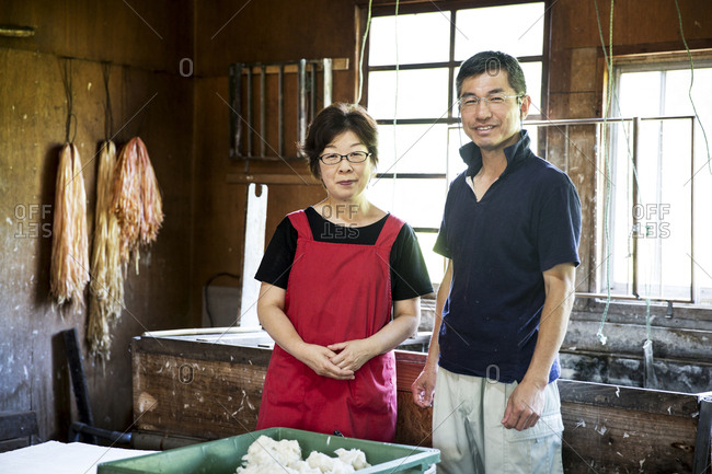 Japanese woman and man standing in a Washi workshop by a vat of pulp, basic plant based ingredients for making paper.