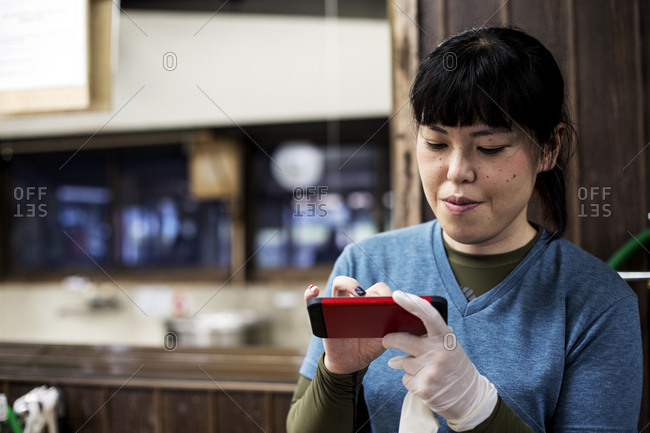 Smiling Japanese woman wearing one glove holding a red smart phone and checking messages.