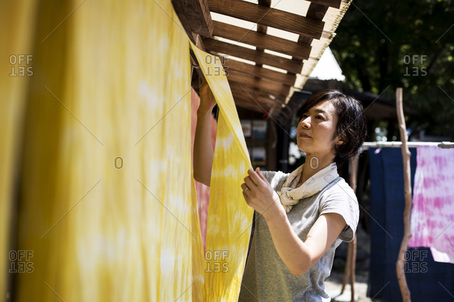 Japanese woman standing in a textile plant dye workshop, hanging up freshly dyed bright yellow fabric.