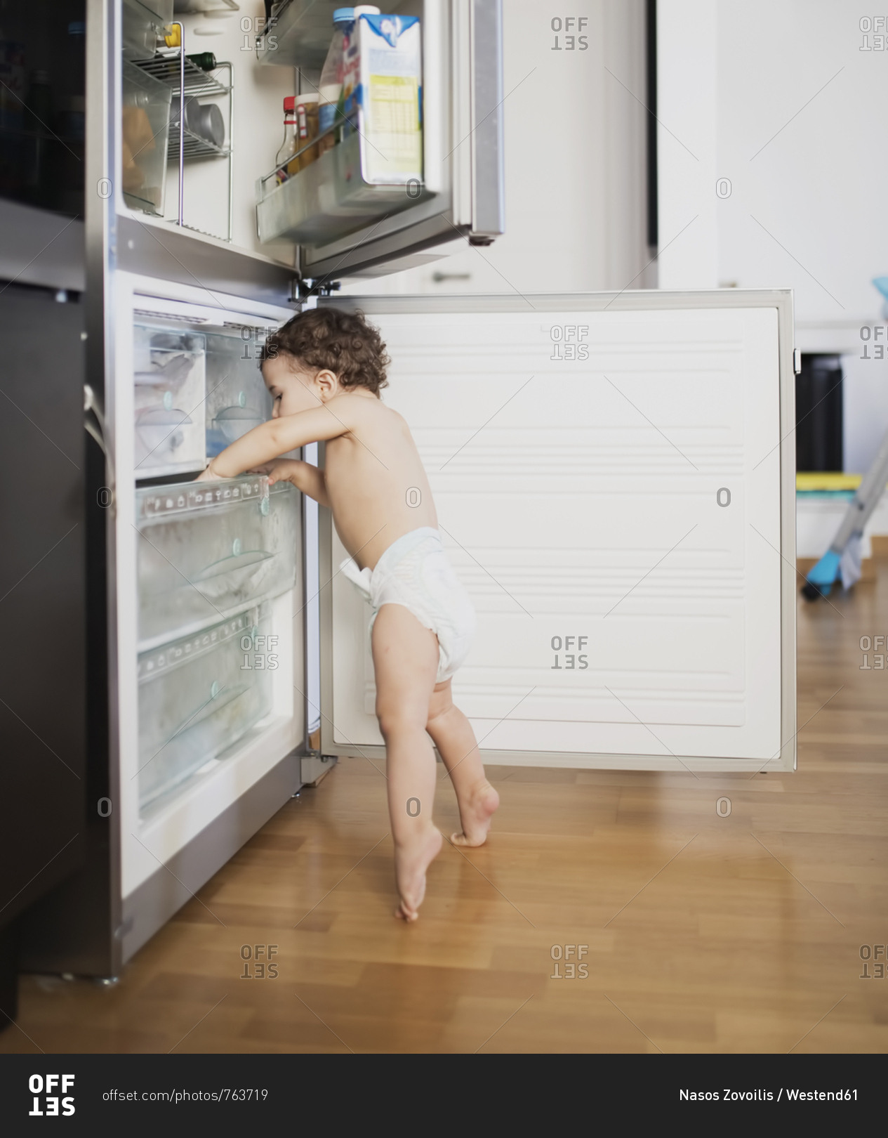 Baby boy wearing diaper exploring refrigerator in the kitchen