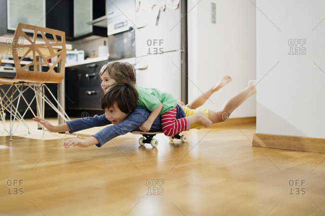 Two brothers at home lying on skateboard together having fun