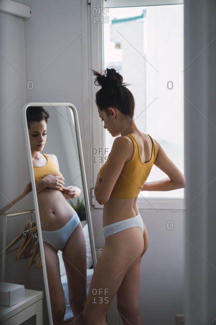 Young woman in underwear at home looking in mirror stock photo - OFFSET
