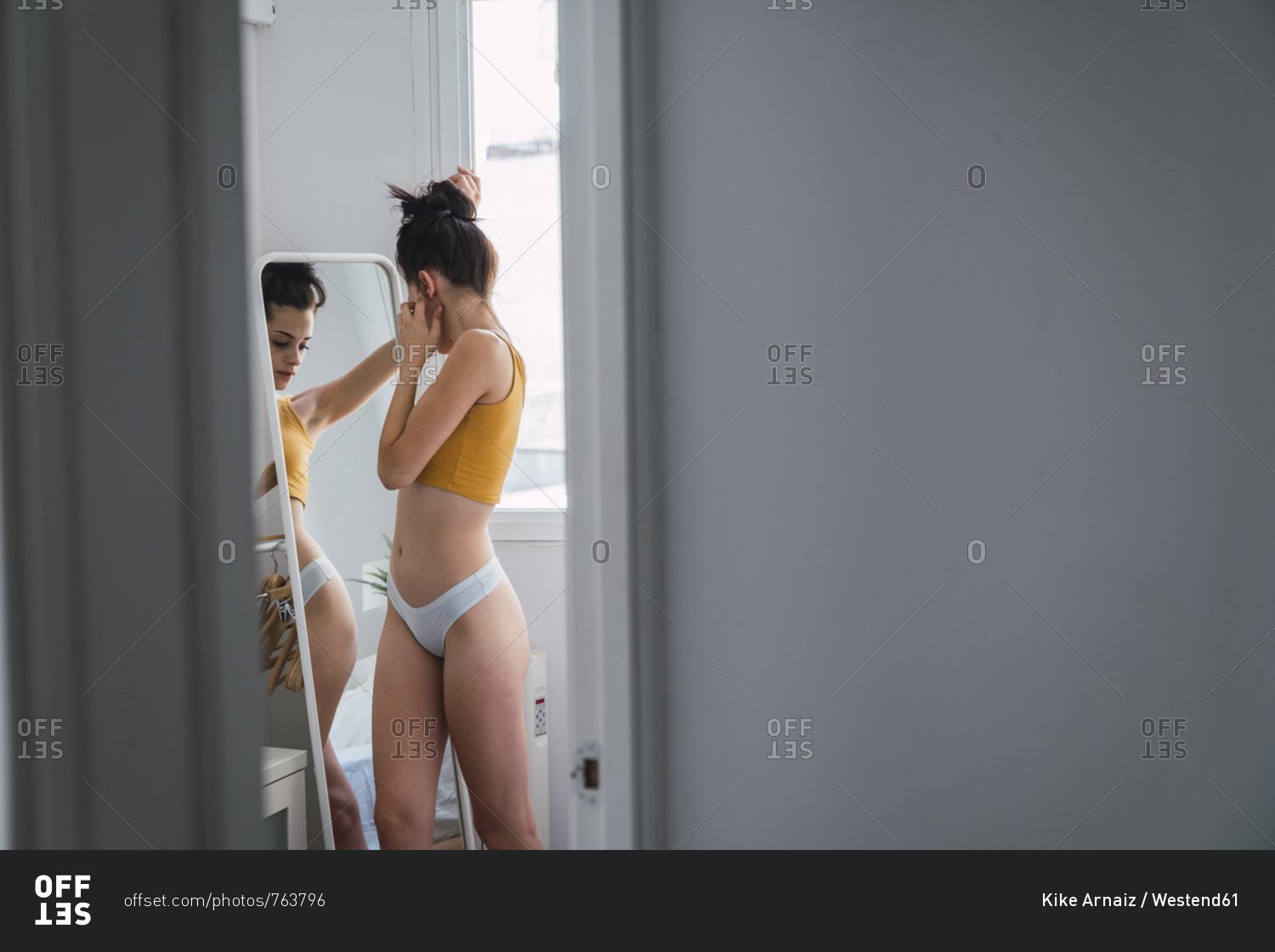 Woman in shirt and panties looking at herself in the mirror of her room  stock photo - OFFSET