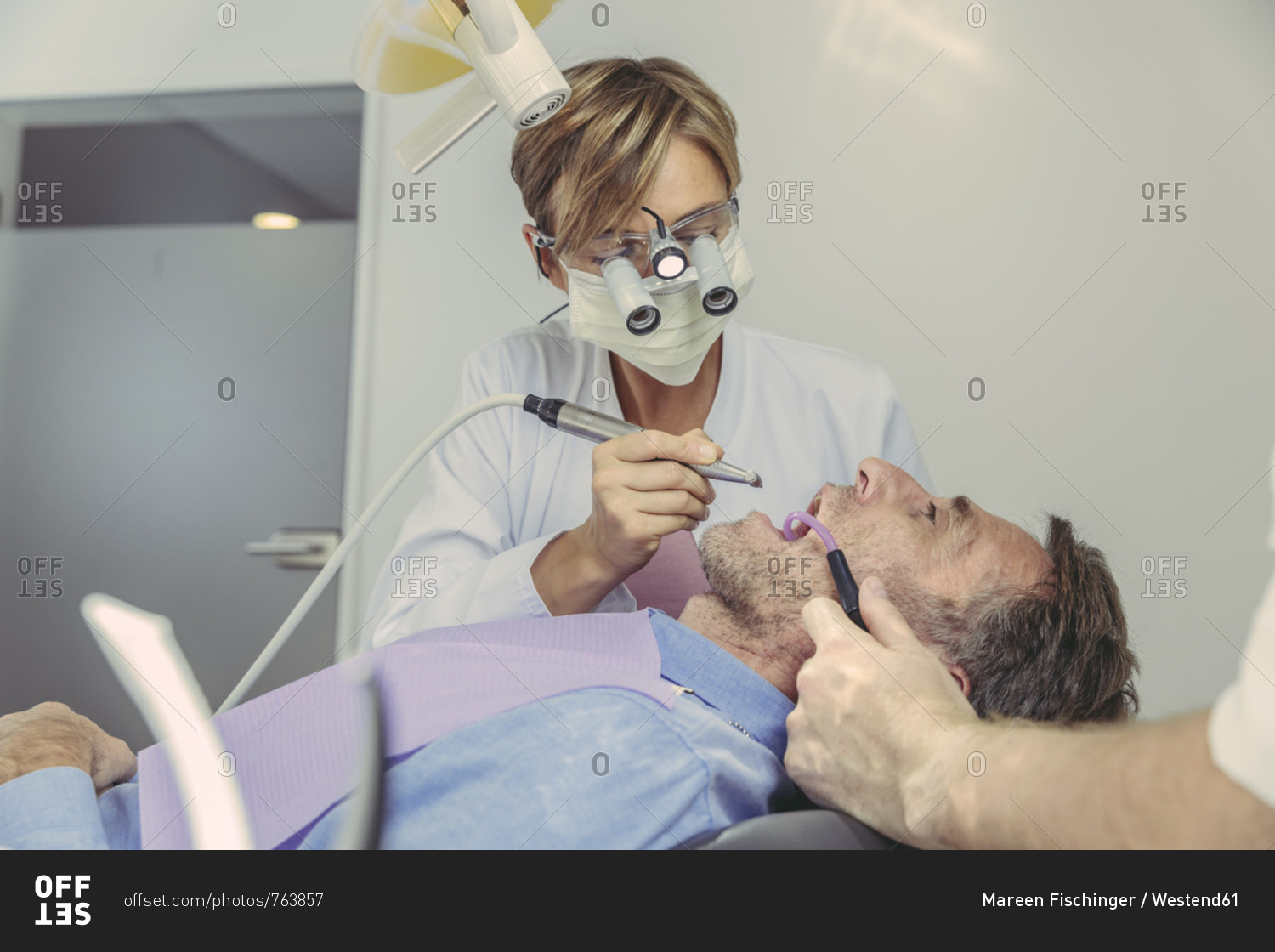 Patient getting dental treatment- dentist using dental drill and head magnifiers and light