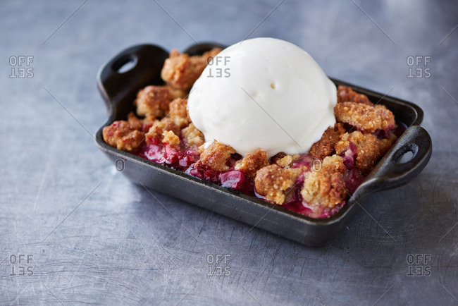 Stonefruit Crumble with peaches and plums, baked in a small cast iron dish and topped with a scoop of vanilla ice cream presented on a stainless steel surface in a farm to table restaurant.