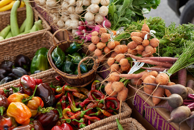 Abundance of produce at an outdoor farmer's market featuring Parisian carrots, peppers and various radishes, displayed for sale at an outdoor farmer's market.