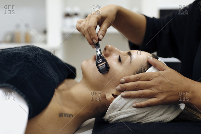 Spa technician using derma roller on woman's face during spa session
