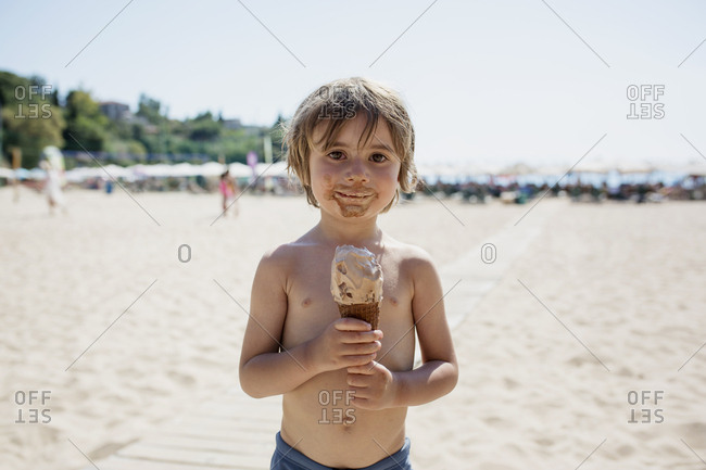 Portrait of messy little boy with ice cream cone standing on the beach