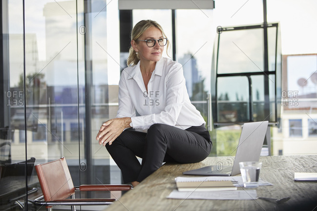 Successful businesswoman sitting on desk- contemplating
