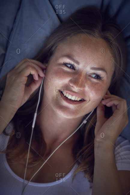 Young woman lying on cushion- listening music with earphones
