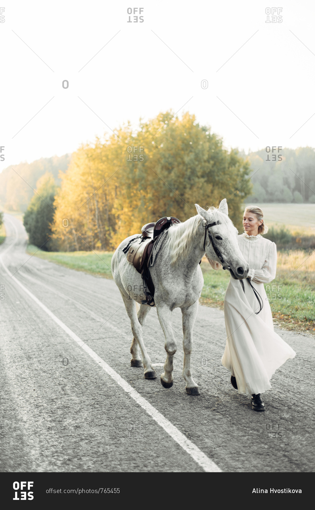 Blonde woman wearing vintage dress walking on country road with horse