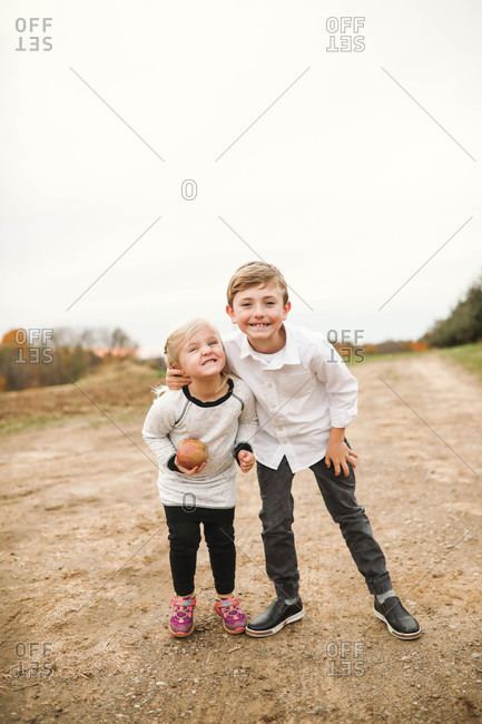 Two blonde siblings standing with arms around each other and making silly smiles