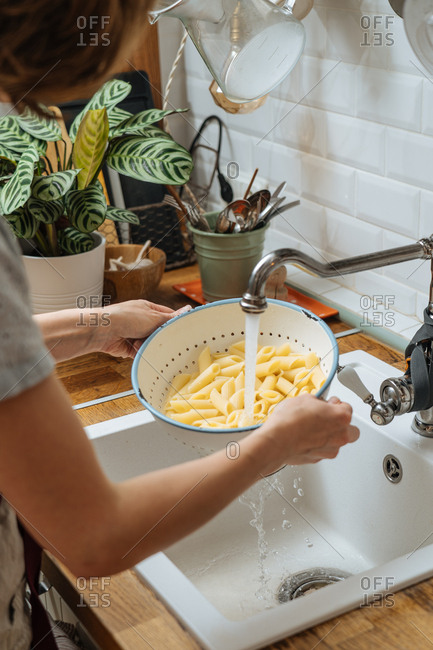 Woman rinsing noodles in a colander in a sink