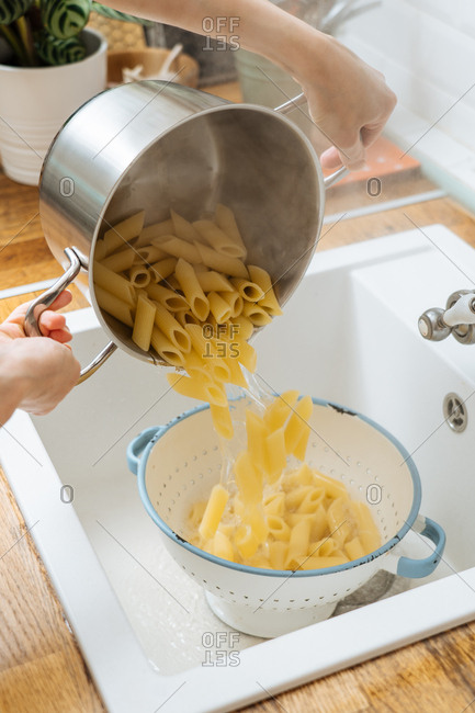 Woman draining noodles in a colander in a sink