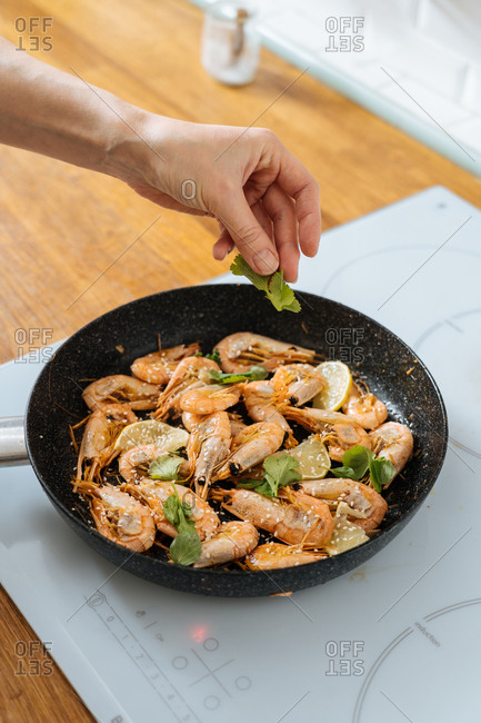 Woman cooking prawns in a skillet with herbs and sesame seeds