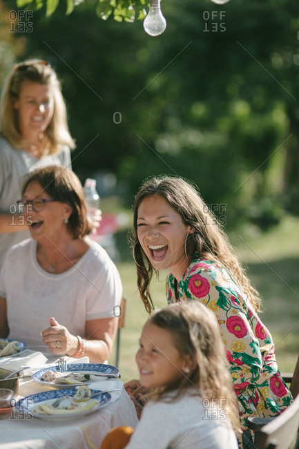 Happy girl having lunch with mother and grandmother at table during garden party