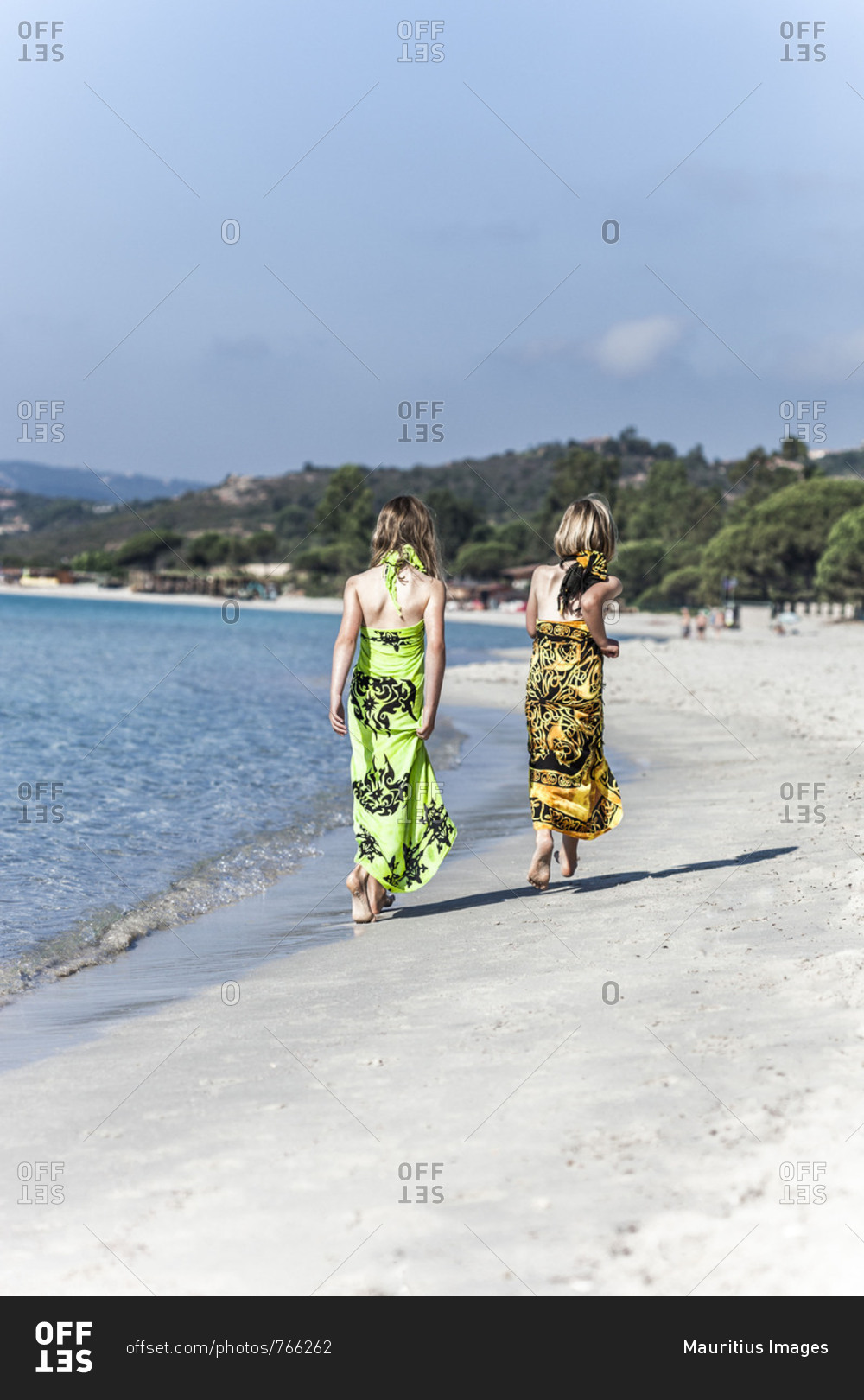 Two girls in beach dresses walking on the sandy, lonely beach of Palombaggia, Corsica
