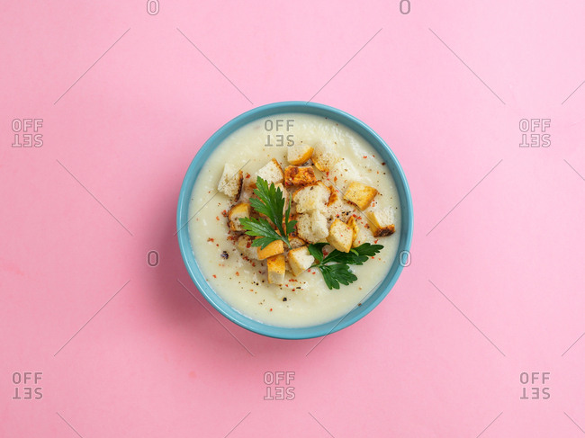 Cauliflower potato soup puree with croutons in blue bowl on pink minimalistic background. Top view flat lay. Copy space