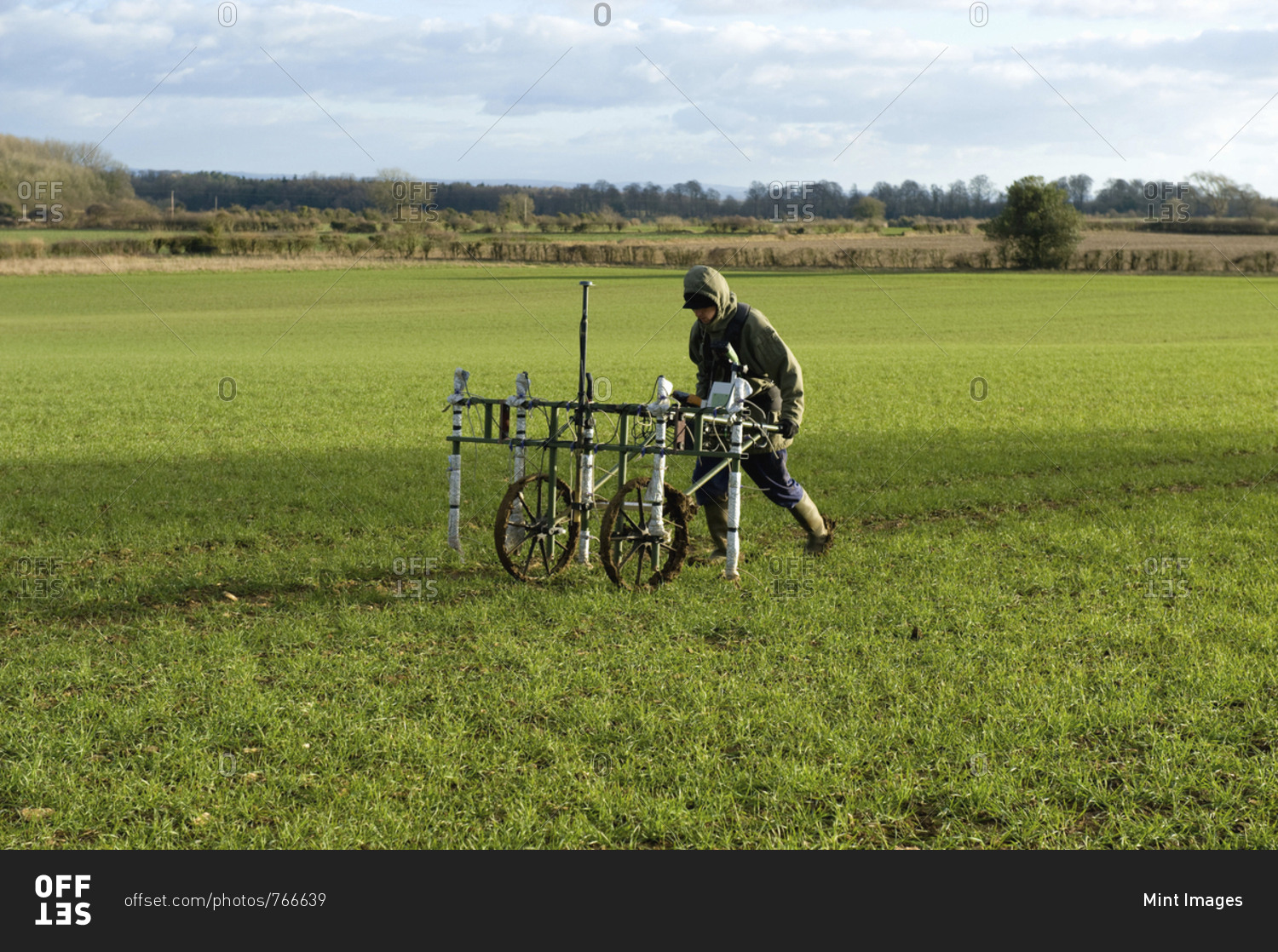 A geophysicist pushing a trolley with ground mapping sensors, creating a geophysical survey of the subsoil in a field.