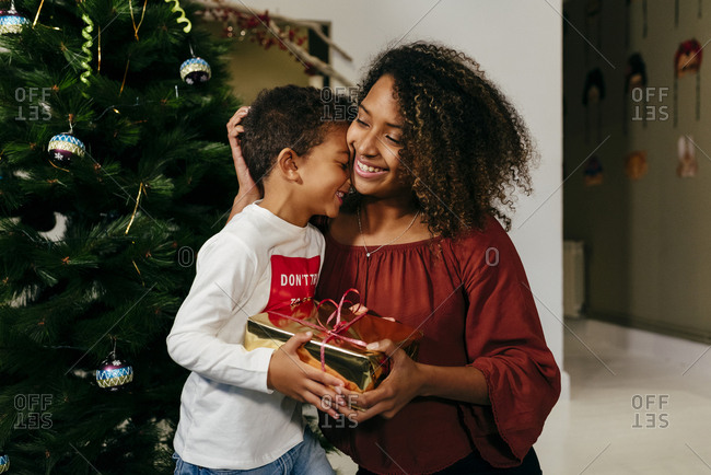 Young black woman giving a gift to a black kid next to the Christmas tree at home