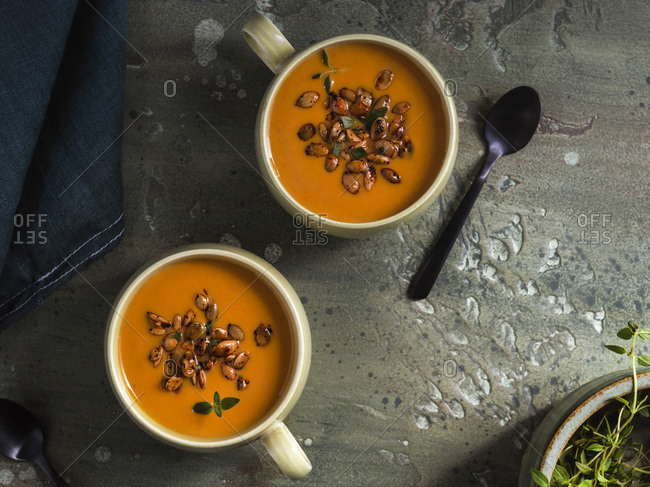 2 vintage, green mugs filled with warm, roasted, pumpkin soup. Garnished with roasted pumpkin seeds and fresh thyme.