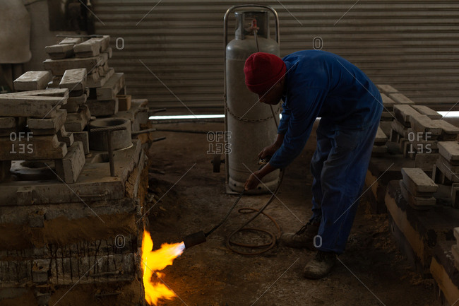 Worker heating furnace with flaming torch in foundry