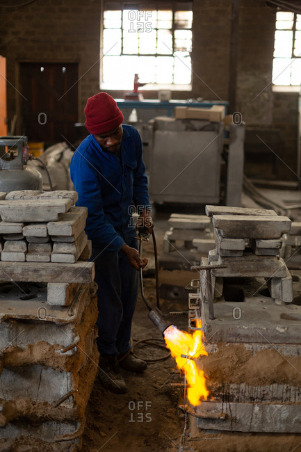 Worker heating furnace with flaming torch in foundry